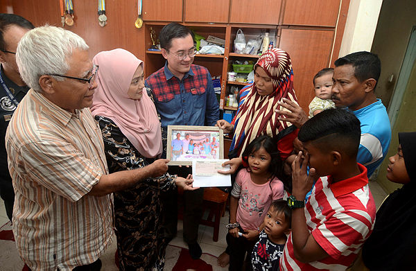 Safety Firtst’s founder Samad Rahim (left) hands over a contribution to Mohamad Hafeiz Mubara, 44, (right) and wife Siti Hajar Ghazali, 38, (fourth from the left) in their house near Sungai Ara today. — Bernama