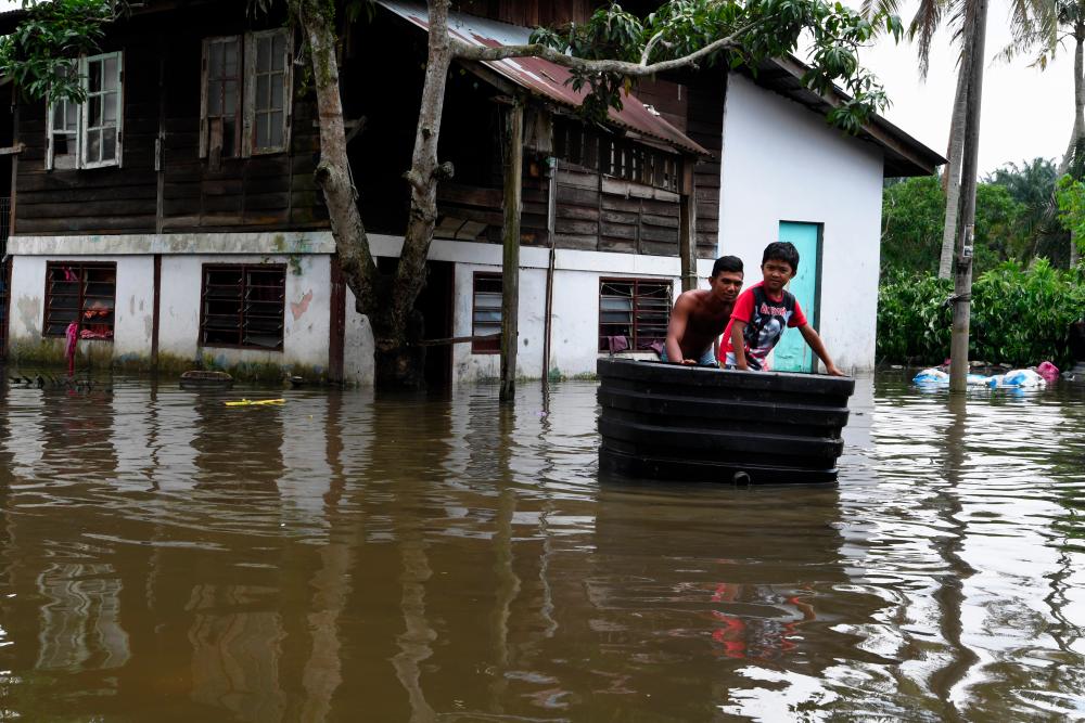 A flood victim using big basin to take a child to safety in Kampung Manggis Permatang Tinggi on Oct 24, 2019. — Bernama