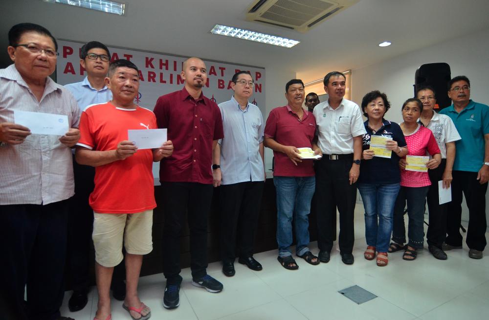 Finance Minister Lim Guan Eng (C) stands with a family whose home was razed to the ground on June 22, at the Bagan DAP service centre today. - Bernama