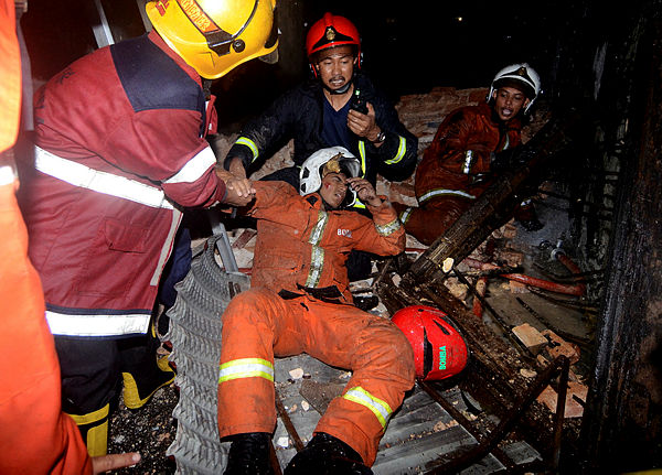 A firefighter is aided by his fellow officers after falling from a building while fighting a fire involving three shophouses in Lebuh Carnavon, George Town. — Bernama