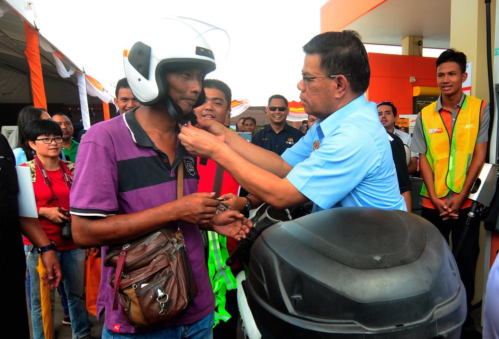 Domestic Trade and Consumer Affairs Minister Datuk Seri Saifuddin Nasution Ismail (2nd from R) fixes a new helmet to a motorcycle rider at the Petroleum Safety Awareness Campaign programme at BH Petrol in Jawi. - Bernama