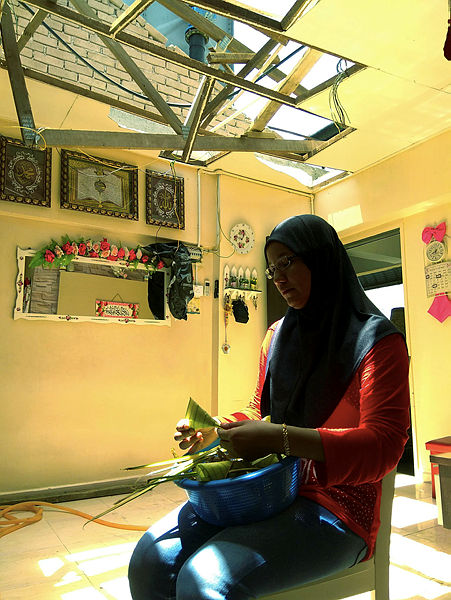 Yusliana Ali, 35, weaves ‘ketupat’ in her home where a storm had caused damage to the roof last night, in Pangsapuri Mutiara Idaman 1. — Bernama