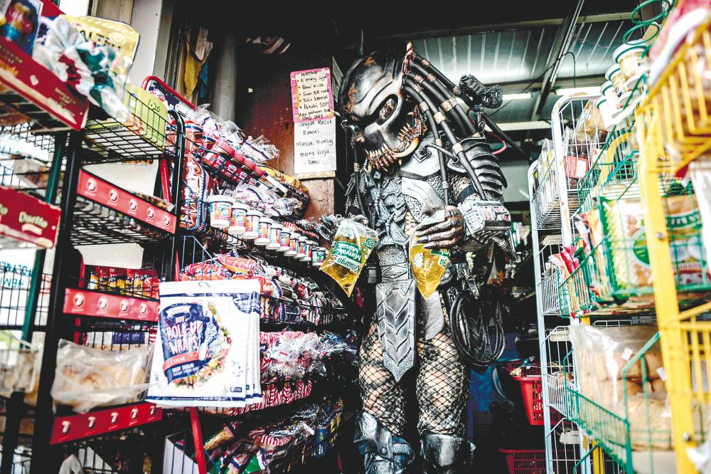 $!CROWD-PULLER ... Mohd Nor Hisham Awang Nong, 47, a disabled street entertainer is seen buying cooking oil before starting his business selling chicken chops in Jalan Utama, George Town yesterday. The father-of-seven said the Predator costume has helped him draw customers. - BERNAMAPIX