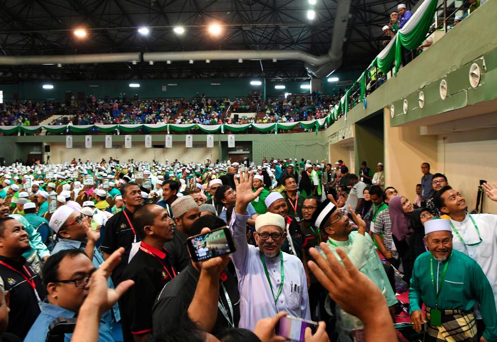 PAS president Datuk Seri Abdul Hadi Awang (C) welcomes and waves to members of the media at the 65th PAS general assembly at the Pahang sports complex in Kuantan today. - Bernama