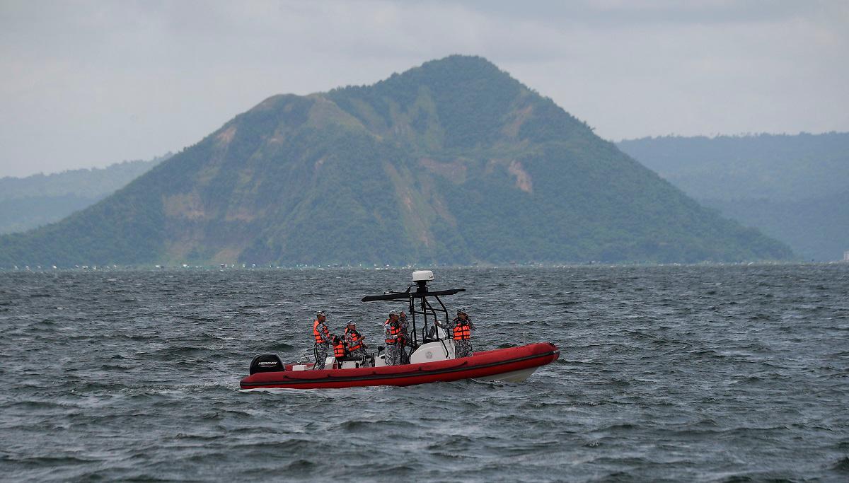 Philippine coast guard personnel aboard an inflatable boat speeds past one of Taal craters on their way to the site where the bodies of cockfighters were allegedly dumped in Taal Lake off Laurel town, Batangas province South of Manila on July 10, 2025. Search teams began scouring a lake south of the Philippine capital Manila for dozens of cockfighters allegedly murdered by rogue police. - Ted ALJIBE / AFP