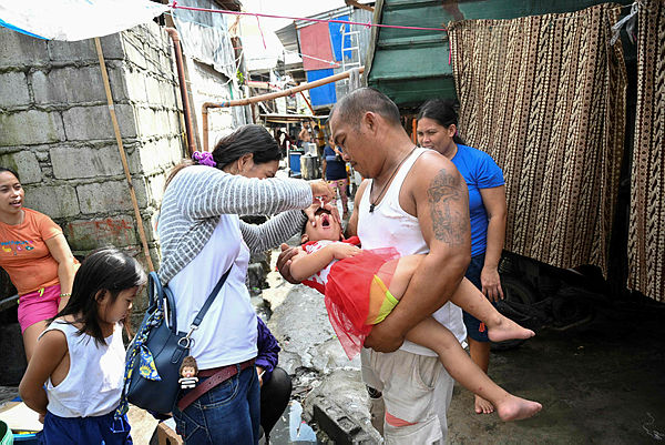 A father watches as a health worker (L) administers polio vaccine on his child during a vaccination drive at an informal settlers area in Manila on October 14, 2019. — AFP
