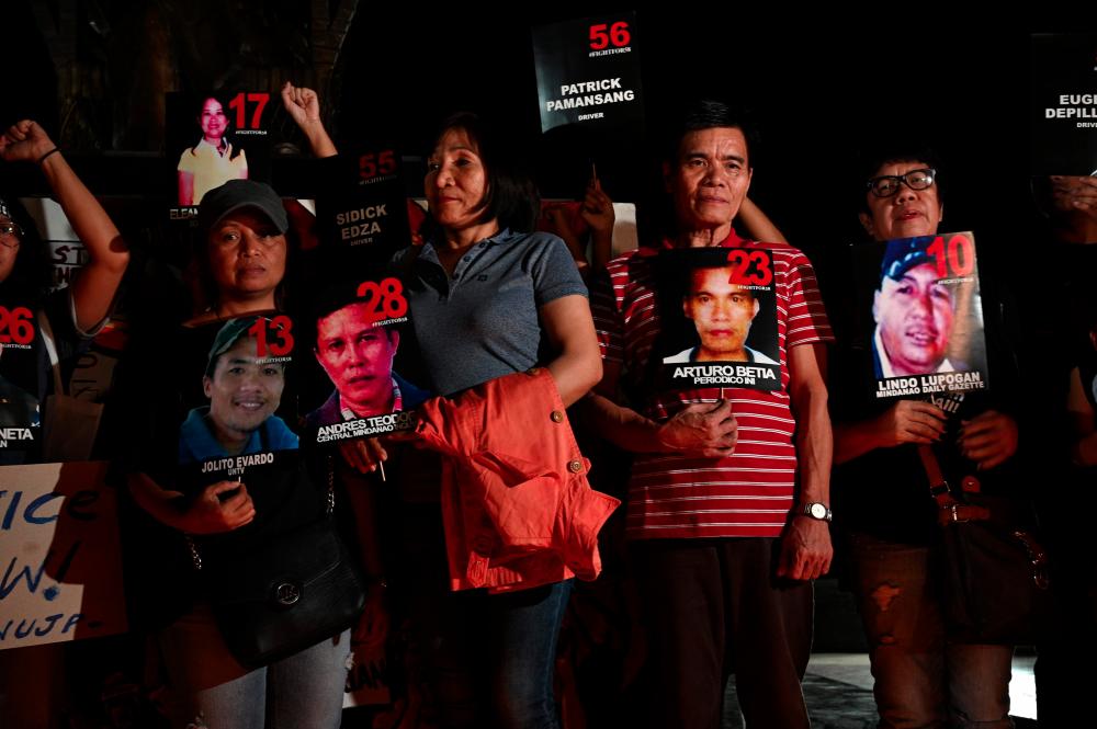 Relatives led by Grace Morales (front, 2nd L), and Gloria Teodoro (3rd L) and supporters of victims of the country's worst political massacre display their photos during a candlelight vigil at a park in Manila on Dec 18, on the eve of a court verdict in the case. — AFP
