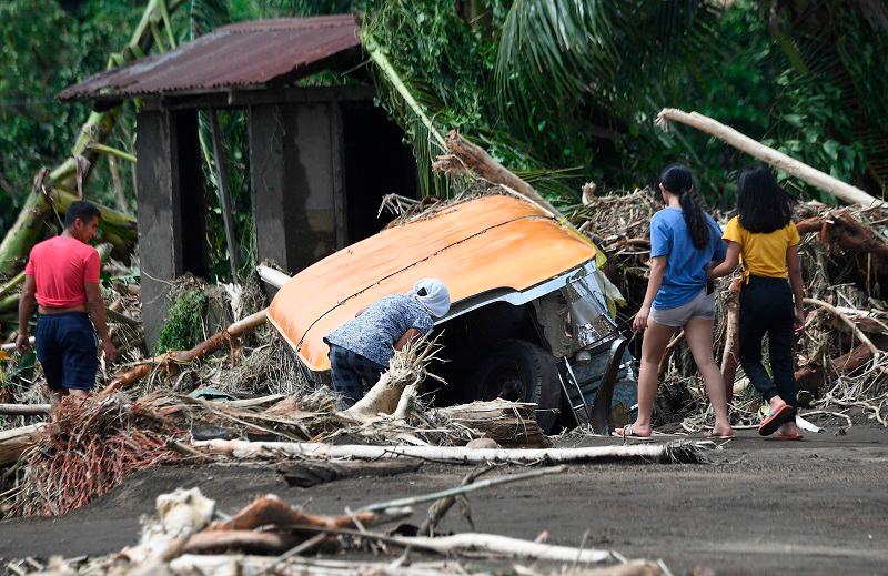 Residents examine a buried passenger jeepney swept away retrieve by floods during heavy rains brought about by Tropical Storm Trami in Laurel town, Batangas province, south of Manila on October 25, 2024. Philippine rescue workers battled floodwaters on October 25 to reach residents still trapped on the roofs of their homes as Tropical Storm Trami moved out to sea after killing at least 40 people. - Ted ALJIBE / AFP