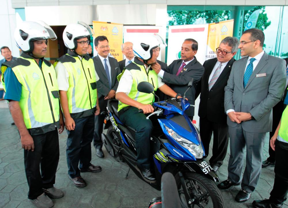 Kula Segaran (third from right) fastens a motorcycle rider’s helmet strap during the National “Safe Driving to Workplace” Campaign 2019 launch.