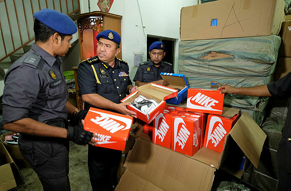 Putrajaya KPDNHEP Investigation Section head Shamsul Nizam Khalil, looking at some of the fake branded shoes seized during the raid in Menglembu last night. — Bernama