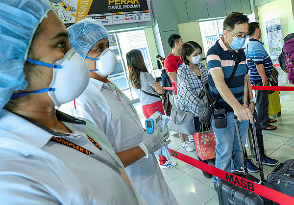 Health officials inspect passengers as they arrive from Singapore at the Sultan Azlan Shah Airport yesterday. — Bernama