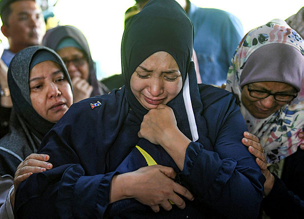 Nour Shafinar Harun (centre), 31, hugs the flag that was given to her after the burial of her husband, Major Mohd Zahir Armaya, 36, at the Tambun Islamic Burial Grounds yesterday. — Bernama