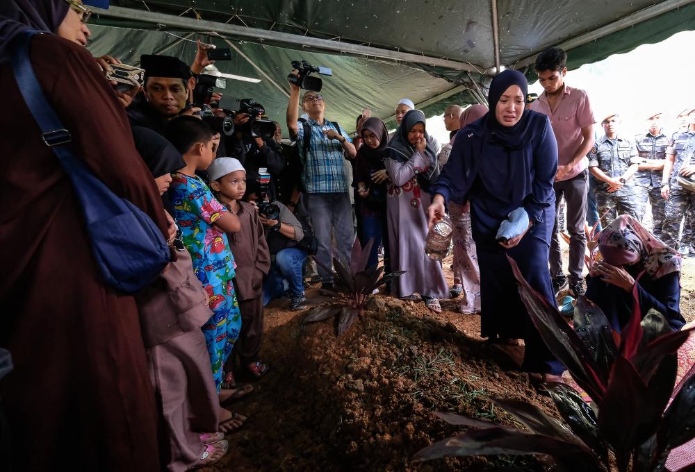 Nour Shafinar Harun, 31, sprays rose water at her husband Major Mohd Zahir Armaya’s grave at the Tambun Muslim Cemetery in Ipoh today. - Bernama
