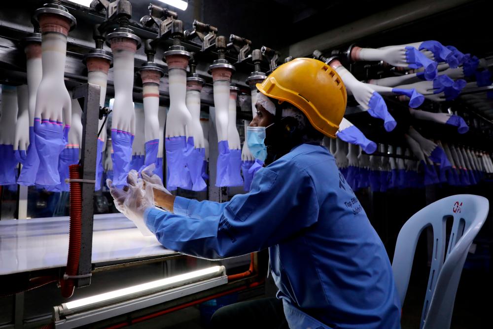 A worker inspects newly made gloves at Top Glove’s factory in Shah Alam. Picture taken in August. – REUTERSPIX