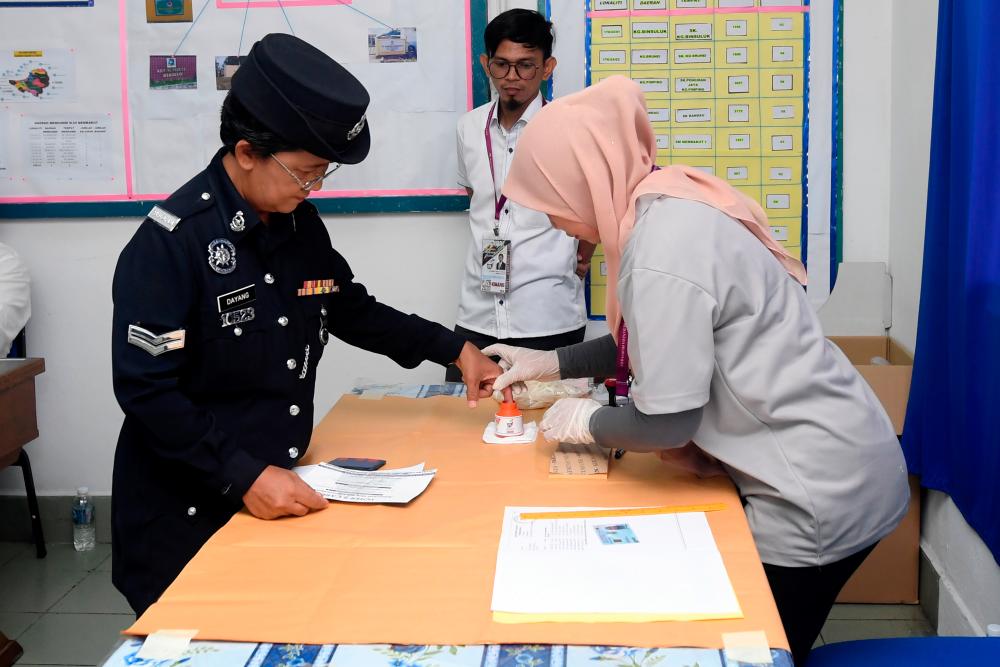 Corporal Dayang Gapah @ Abdullah (L) is assisted by an EC officer while voting early at the operation room in the Membakut police station for the Kimanis by-election. - Bernama