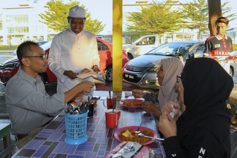 N24 Semenyih candidate, Muhammad Aiman ​​Zainali (2L) distributes the campaign pamphlets to local residents at Warung Nasi Lemak Omak Den Batu 2, on Feb 21, 2019. — Bernama