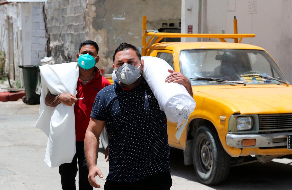 Workers wearing protective masks transport rolls of fabric on a street in Qatar's capital Doha, on May 17, 2020, as the country begins enforcing the world's toughest penalties for failing to wear masks in public while it battles one of the world's highest coronavirus infection rates. — AFP