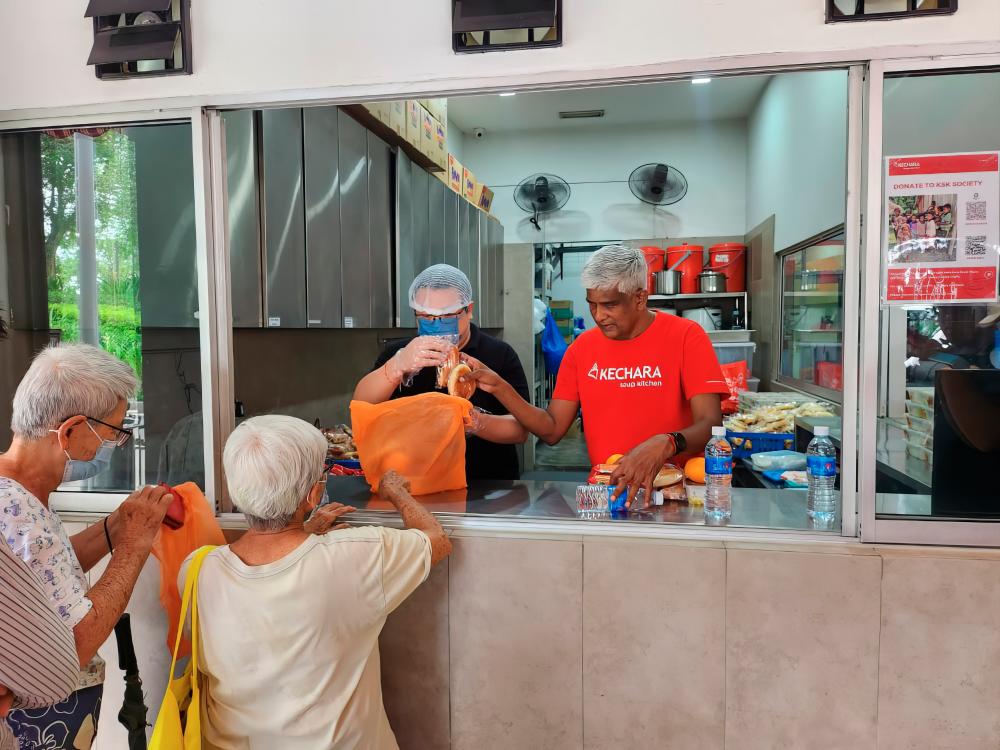 Lee (left) and Selladurai handing out food at Kechara Soup Kitchen. — PIC BY JOHNTAN/THESUN