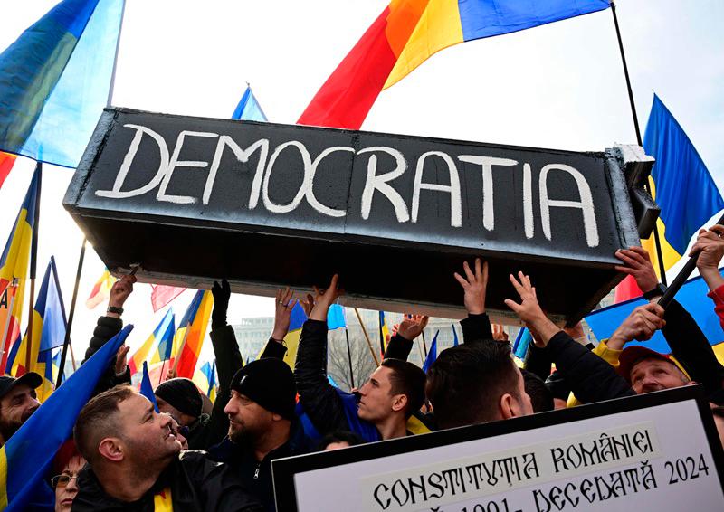 People carry a mock-up coffin reading Democracy during a protest in front of Romania's Constitutional Court in Budapest on January 10, 2024, as thousands of supporters of presidential candidate Calin Georgescu rally to protest against the annullement of the second tour of the presidential election, asking the decision to be reversed. Romania has been in crisis after presidential elections were cancelled in December 2024 -- a hugely unusual move in Europe -- after the far-right candidate Georgescu scored a surprise first-round victory amid claims of Russian interference. The hitherto little-known Calin Georgescu is contesting the annulment in the courts, accusing the authorities of a formalised coup d'etat. - Daniel MIHAILESCU / AFP