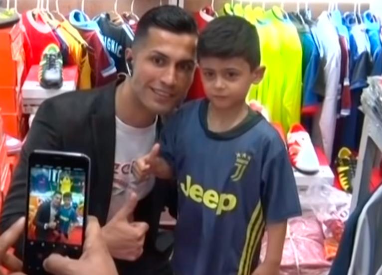 Biwar Abdullah, basking in the limelight, poses with a kid donned in Juventus jersey in a shop selling replica shirt of football teams.