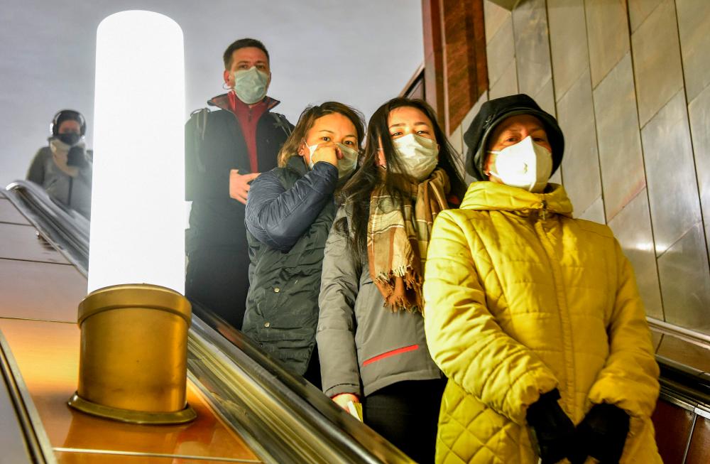 People wearing face masks ride down an escalator at the Moscow metro on March 30, as the city goes on lockdown to stop the spread of Covid-19 (novel coronavirus). - AFP