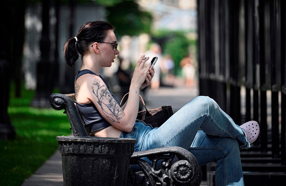 A girl uses her smart phone as she holds a urinating dog on a leash in Moscow on July 30, 2025. - Alexander NEMENOV / AFP