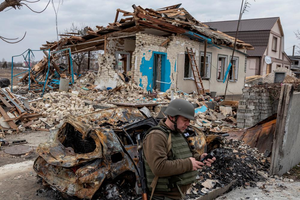 A Ukrainian serviceman checks his mobile phone in front of a destroyed house, as Russia's attack on Ukraine continues, in the village of Krasylivka outside Kyiv/REUTERSPix