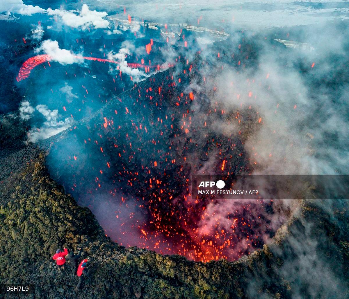 A picture taken with a drone on March 16, 2021 shows members of a local search and rescue squad taking pictures of Klyuchevskoy volcano eruption on Russia's far eastern Kamchatka peninsula. - Maxim FESYUNOV / AFP