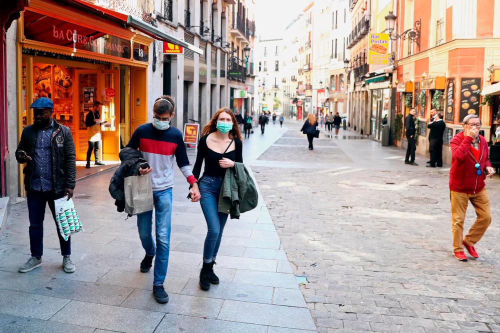 A couple wear protective face masks as they walk in unusually quiet Postas street in central Madrid, Spain, March 13, 2020. -Reuters