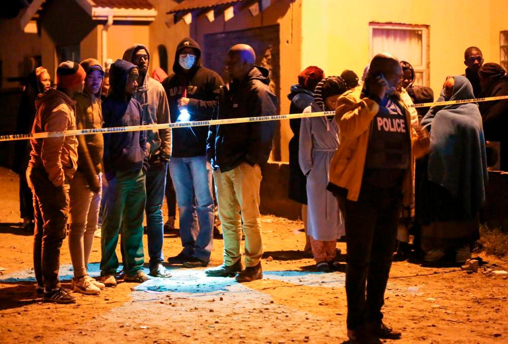 Members of the community and family wait for news outside a township pub as a police officer talks on a phone in South Africa’s southern city of East London on June 26, 2022, after 20 teenagers died/AFPPix