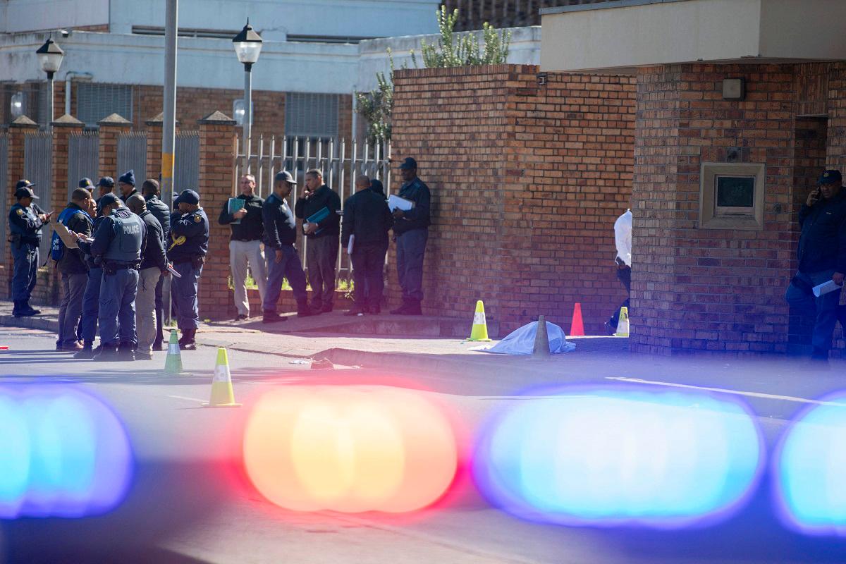 Members of the South African Police Services (SAPS) stand next to the body of a young man who had been shot shortly before outside the Mitchells Plain Magistrates Court near Cape Town on August 25, 2025. - RODGER BOSCH / AFP