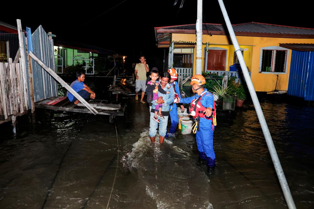 SANDAKAN, 25 Dis -- Anggota Pertahanan Awam (APM) membantu penduduk melalui jambatan yang sudah ditenggelami air laut untuk berpindah ke tempat selamat sewaktu membuat pemantauan fenomena air pasang besar di Kampung Tinusa Dua malam tadi. fotoBERNAMA