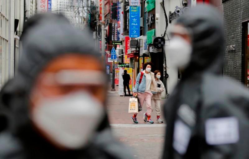 Pedestrians wearing masks are seen behind South Korean soldiers doing quarantine works, following the rise in confirmed cases of coronavirus disease (Covid-19) in Daegu, South Korea, March 15, 2020. — Reuters