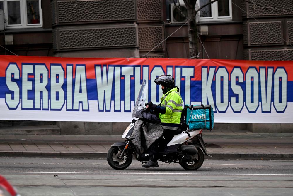 A delivery scooter conductor drives past a banner placed across the Serbian government building, in Belgrade on January 23, 2023. AFPPIX