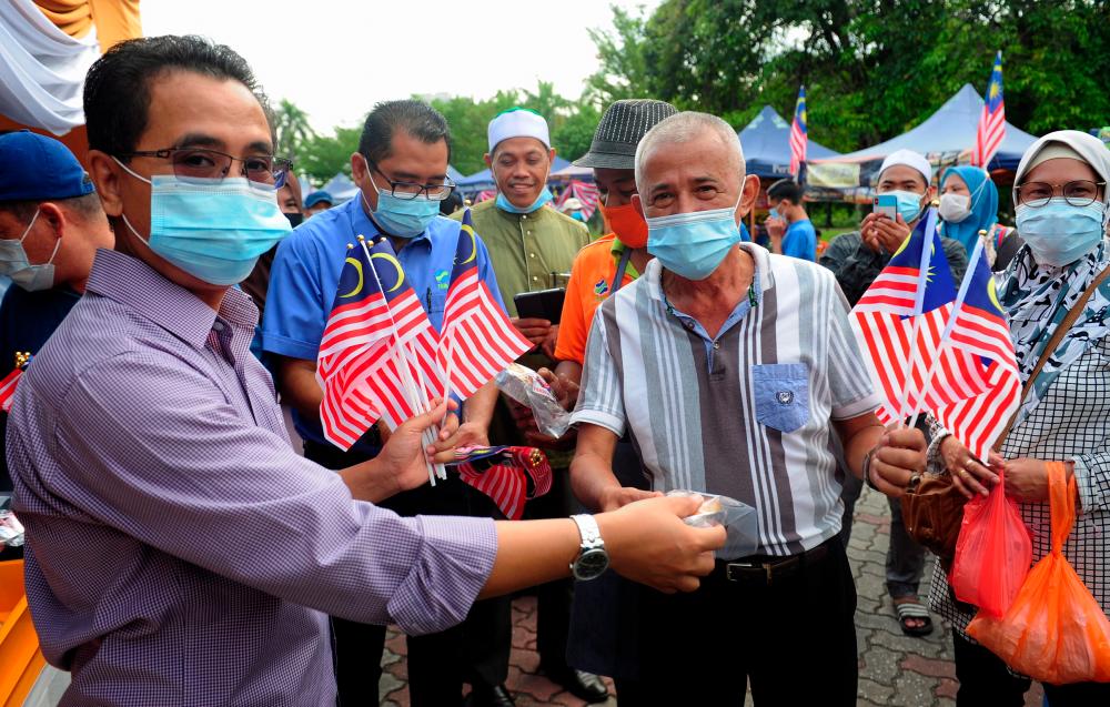 Selangor Federal Agricultural Marketing Authority (Fama) director Abdul Rashid Bahri (L) distributes Jalur Gemilang at the 63rd Independence Day and Fly the Jalur Gemilang campaign at the Shah Alam Stadium Farmers’ Market today. — Bernama