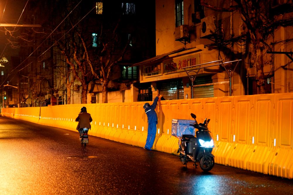 FILE PHOTO: An Ele.me delivery worker hands a bag to a resident behind barriers sealing off an area, before the second stage of a two-stage lockdown to curb the spread of the coronavirus disease (Covid-19) in Shanghai, China, March 31, 2022. REUTERSpix