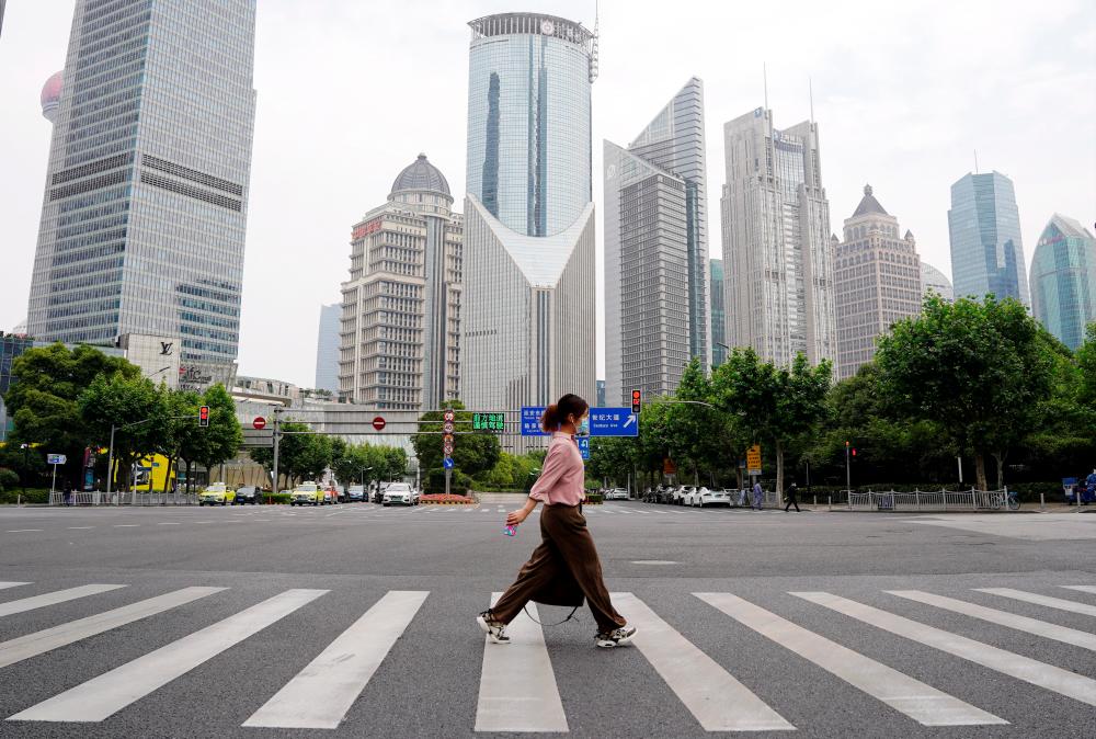 File photo: A pedestrian wearing a face mask crosses a road in front of office towers in Lujiazui financial district, after the lockdown placed to curb the coronavirus disease (Covid-19) outbreak was lifted in Shanghai, China June 1, 2022. REUTERSpix