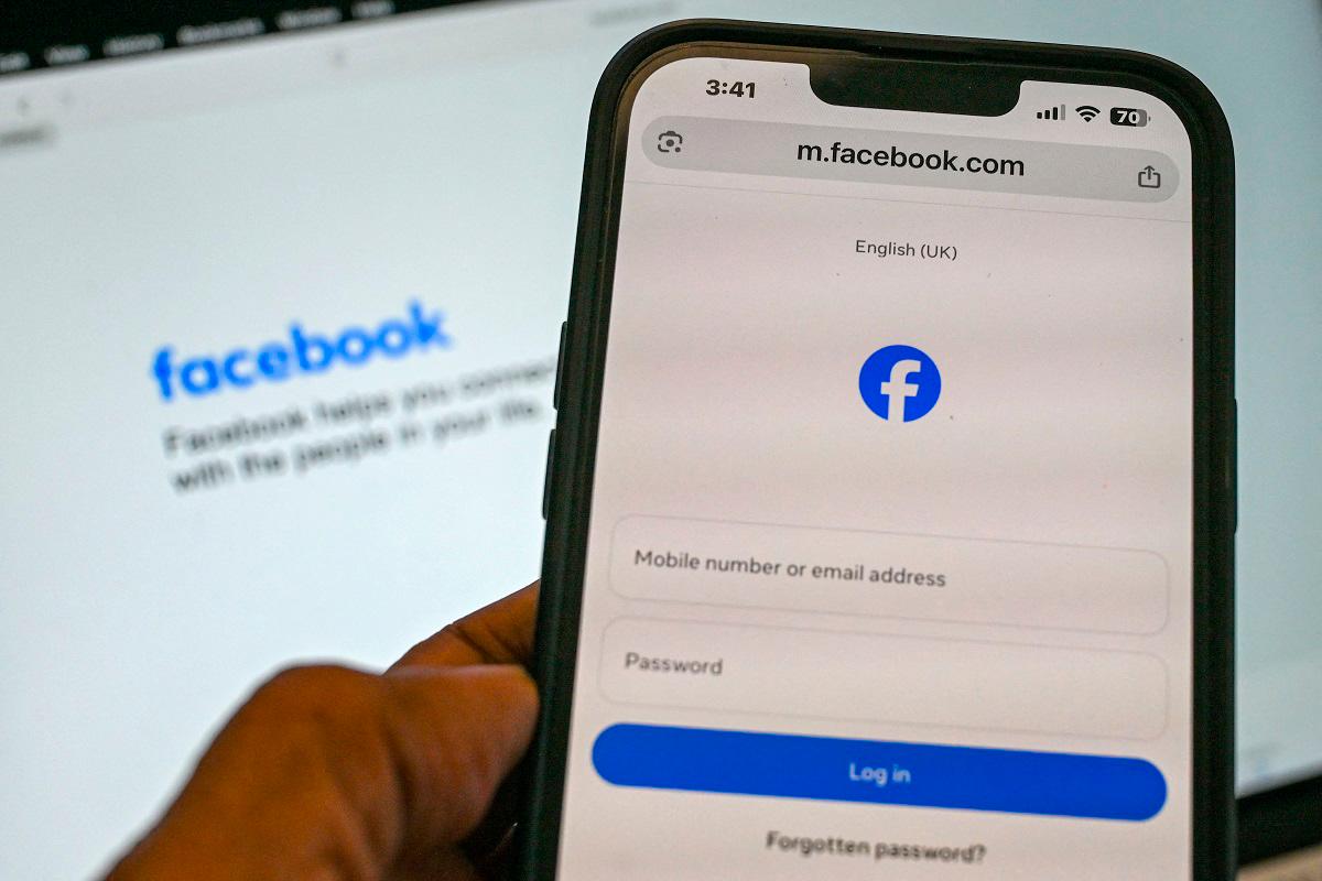 An illustration photograph taken on September 3, 2025 shows a person holding a phone on the Facebook log-in page in Singapore. - Roslan RAHMAN / AFP