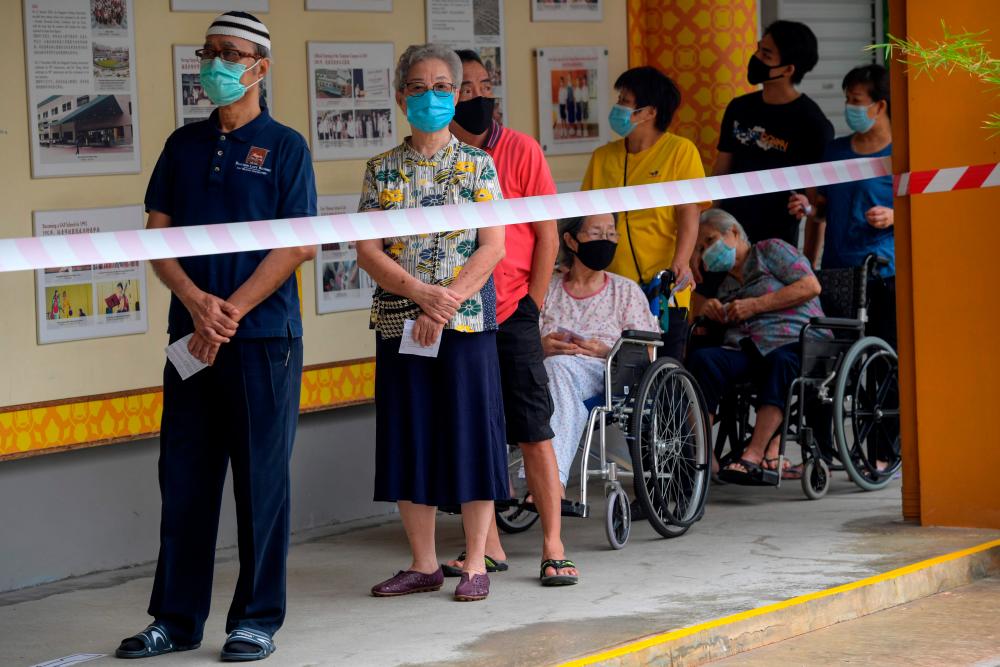 Voters wearing face masks wait to cast their ballots during the general election in Singapore on July 10, 2020. — AFP