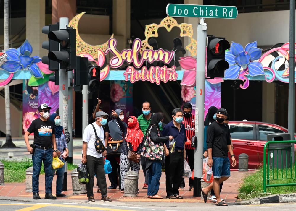 People wearing face masks amid concern over the spread of the Covid-19 coronavirus wait at a road crossing with building displays of festive decorations ahead of Eid al-Fitr which marks the end of the Muslim holy month of Ramadan, at the Geylang Serai market in Singapore on May 21, 2020. - AFP