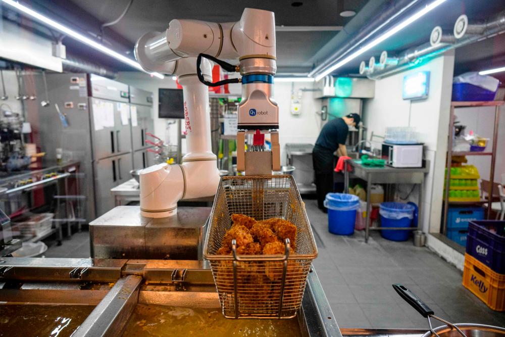 In this photo taken on June 13, 2023, a robot fries chicken as an employee washes dishes at a Robert Chicken restaurant in Seoul. AFPPIX