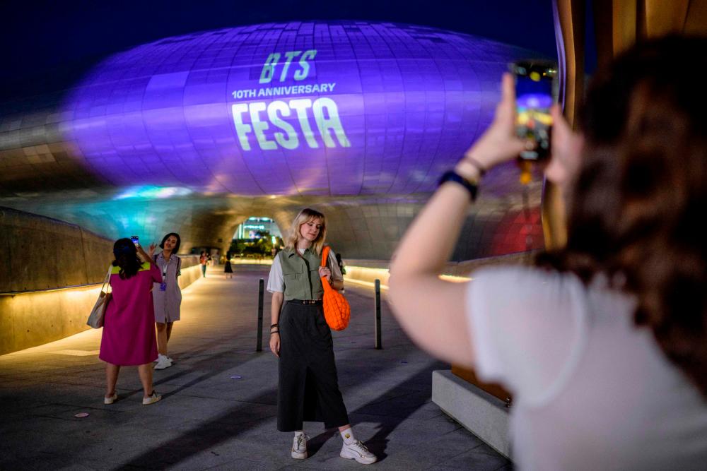 A fan poses for photos in front of the Dongdaemun Design Plaza as it is illuminated in purple light to mark the 10-year anniversary of K-pop megastars BTS, in Seoul on June 12, 2023. AFPPIX