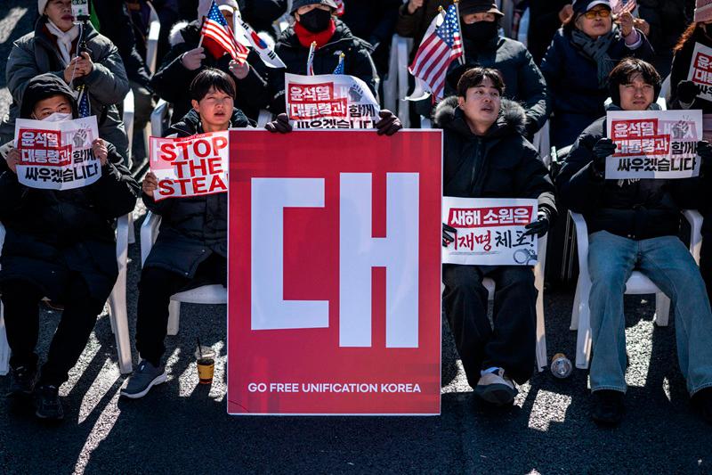 Demonstrators sit beside a board that reads Go Free Unification Korea (C) during a rally in support of impeached South Korea president Yoon Suk Yeol in the Gwanghwamun area of Seoul on January 4, 2025. South Korea's political leadership was in uncharted territory January 4 after the sitting president resisted arrest over a failed martial law decree days before the warrant expires. (Photo by Philip FONG / AFP)