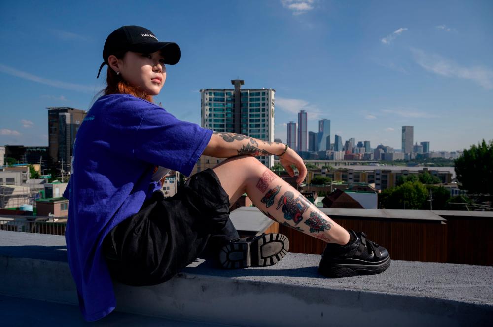 In a photo taken on September 4, 2020 tattoo artist Seo Uri poses for a photo before the city skyline of Seoul. In South Korea while tattooing itself is not illegal, it is classed as a medical procedure and may only be carried out by a fully qualified doctor -- with up to two years in prison for violators. / AFP / Ed JONES /