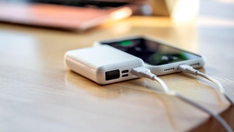 The smartphone is charged from a small white power bank via a cord.