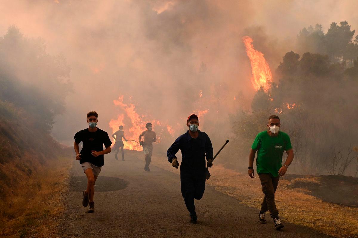 People run by a burnt area during a wildfire near the village of Larouco, in the province of Ourense, in northwestern Spain on August 13, 2025- AFP