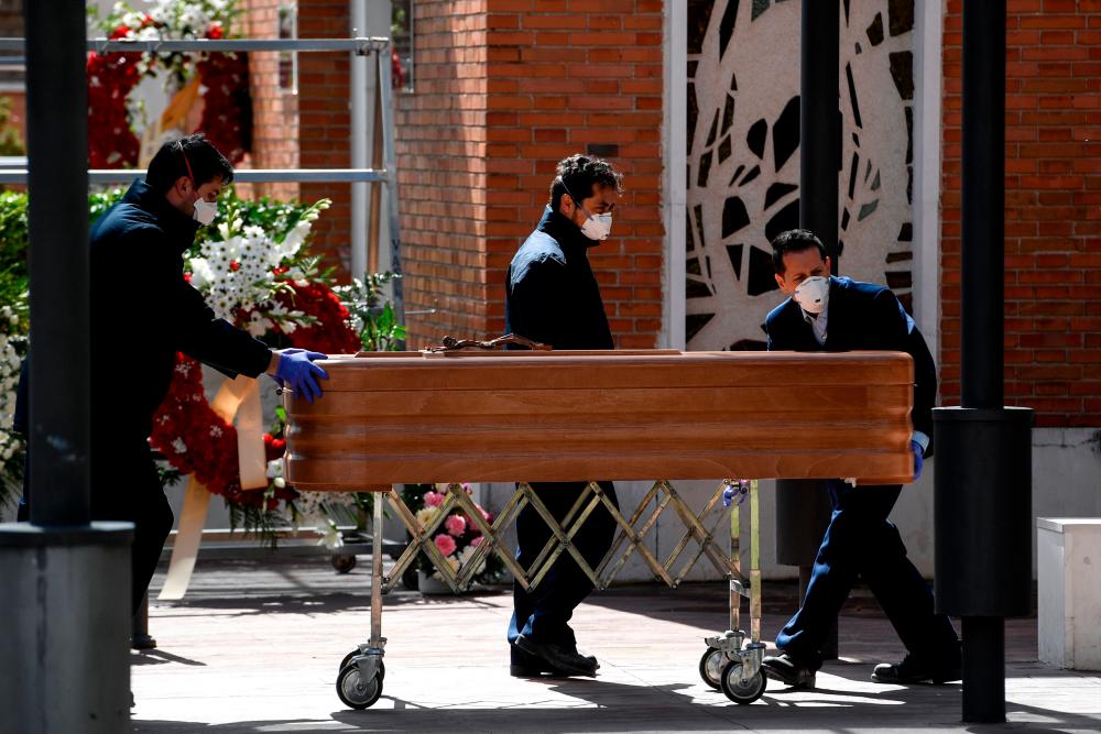 Mortuary employees wearing face masks wheel a coffin into the crematorium of La Almudena cemetery in Madrid on March 24, 2020 during the funeral of a COVID-19 coronavirus victim. - AFP