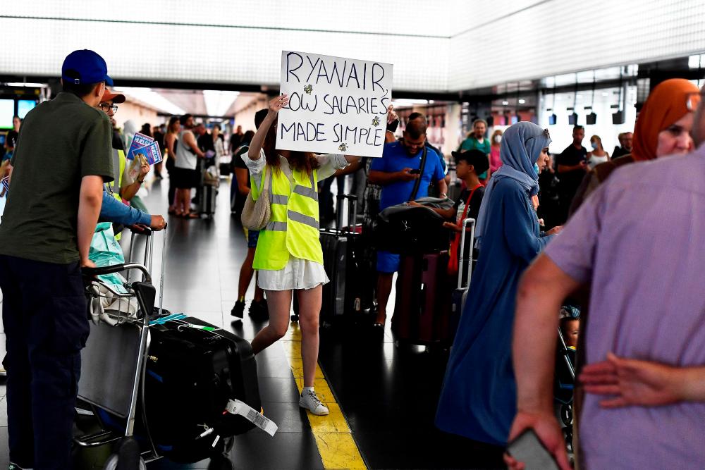 A woman holds a placard reading “Ryanair, low salaries made simple” as she protests at the Terminal 2 of El Prat airport in Barcelona on June 24, 2022/AFPPix