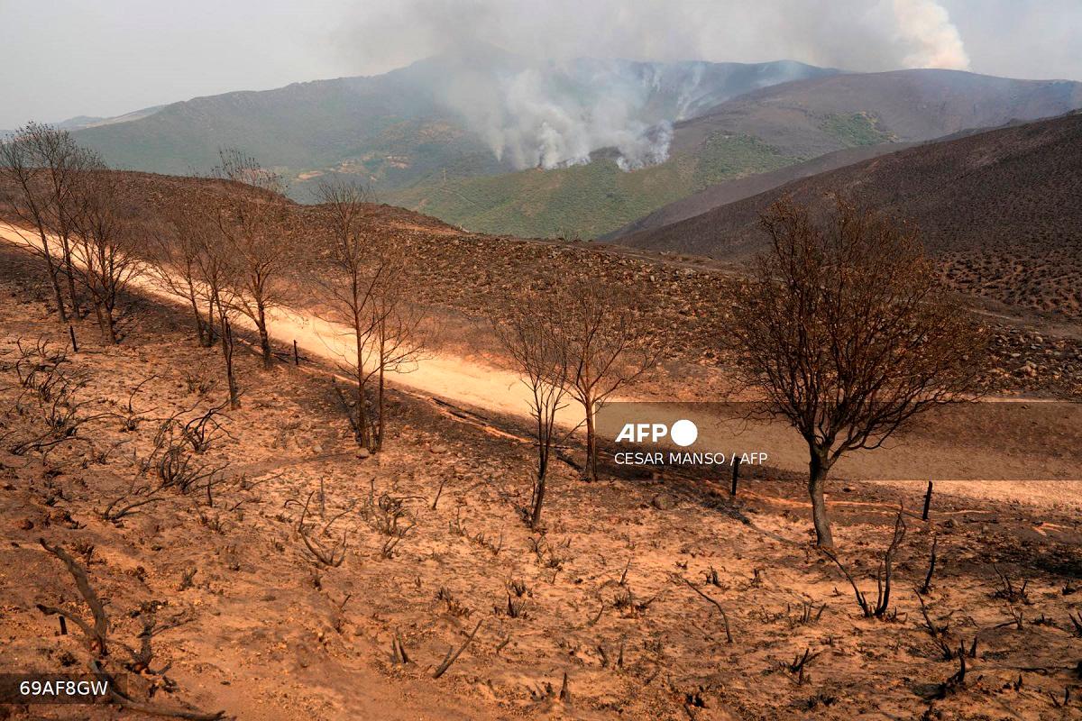This picture taken from a burned area at the Orellana viewpoint in the Roman-era mining site of Las Medulas in the municipality of Carucedo, shows a wildfire in the background, on August 11, 2025. - Cesar Manso / AFP