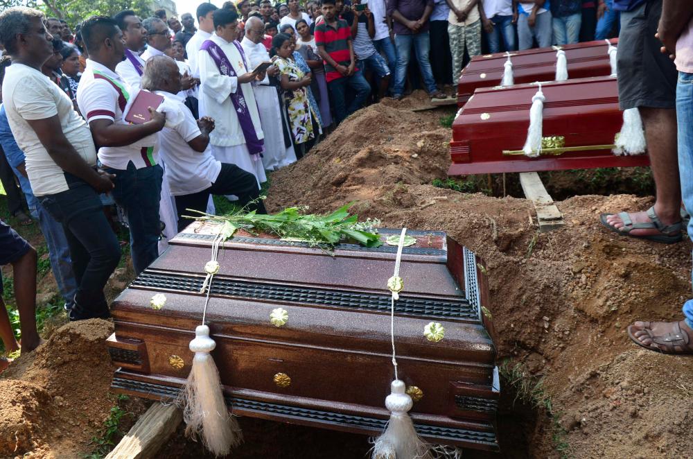 A priest (L) administrates a burial ritual for a bomb blast victim in a cemetery in Colombo on April 23, 2019, two days after a series of bomb attacks targeting churches and luxury hotels in Sri Lanka. — AFP